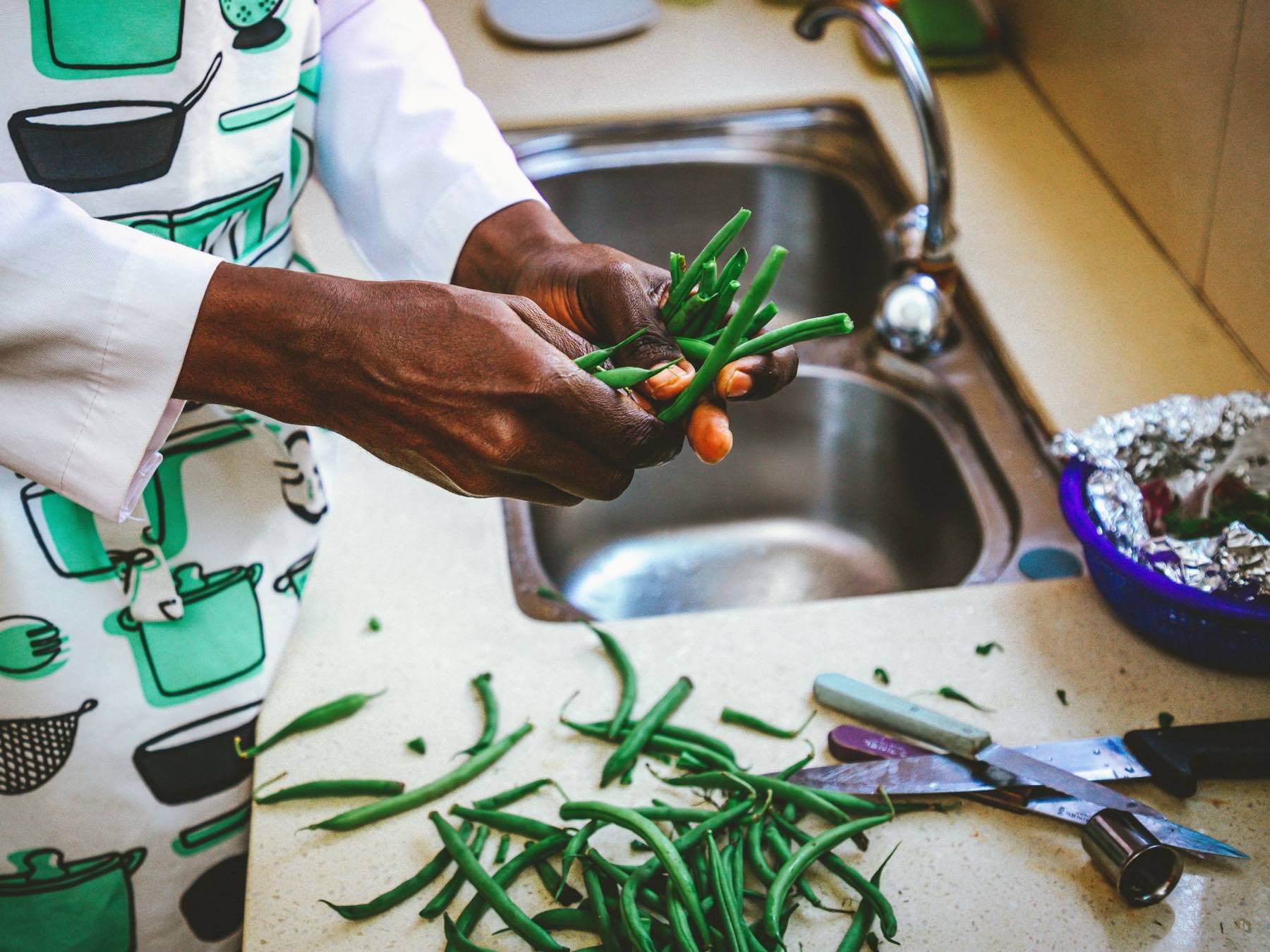 Hands topping and tailing green beans at a kitchen sink